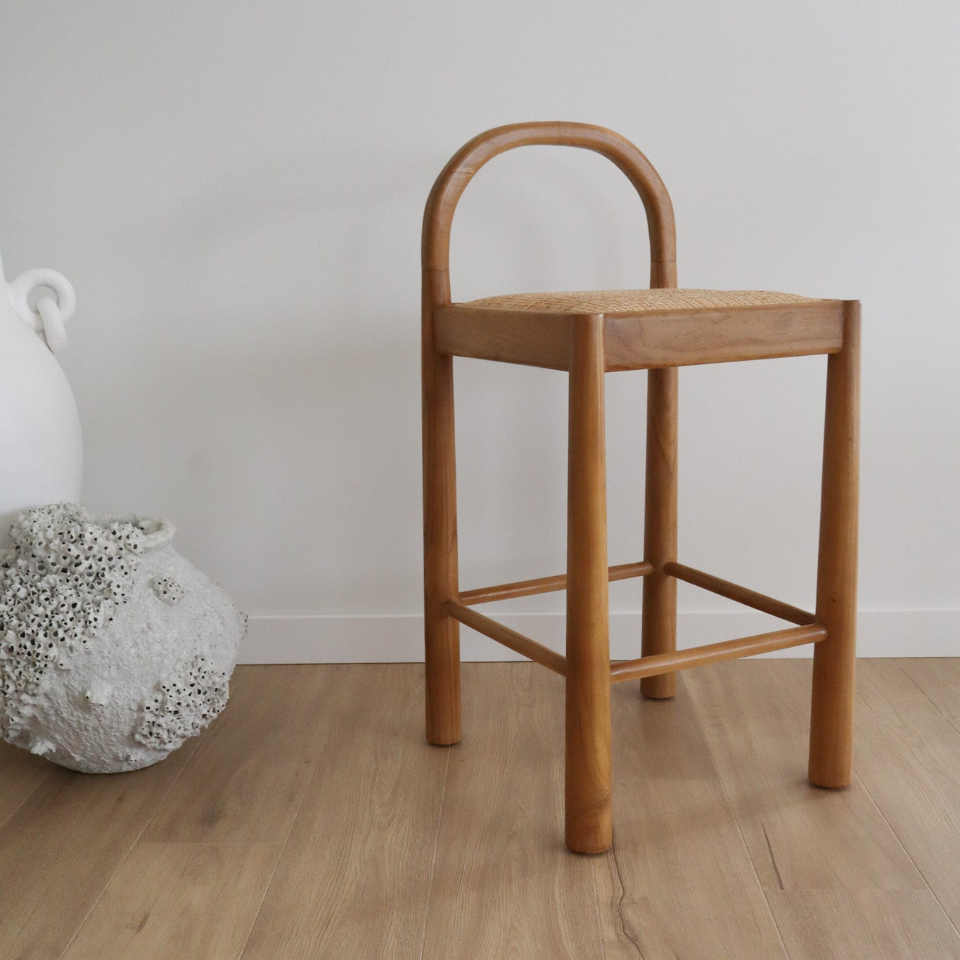 Wooden bar stool against a plain wall with decorative elements on a wooden floor.