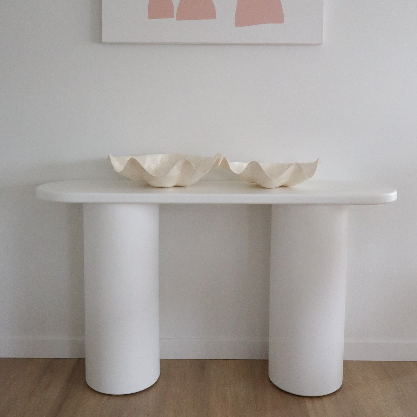 White table with two decorative bowls against a light gray wall with abstract pink art.
