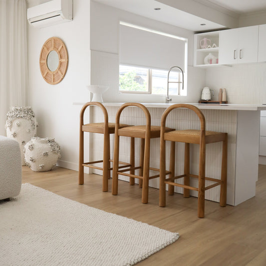 Modern kitchen with wooden bar stools, white cabinets, and a rug on the floor.